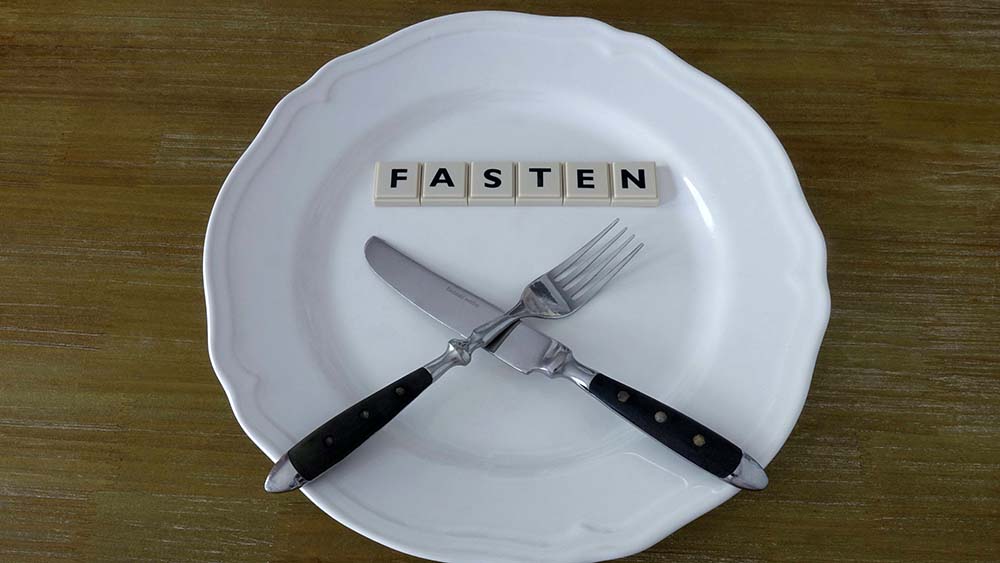Leerer Teller mit Messer und Gabel, Buchstaben mit dem Wort "Fasten" darüber