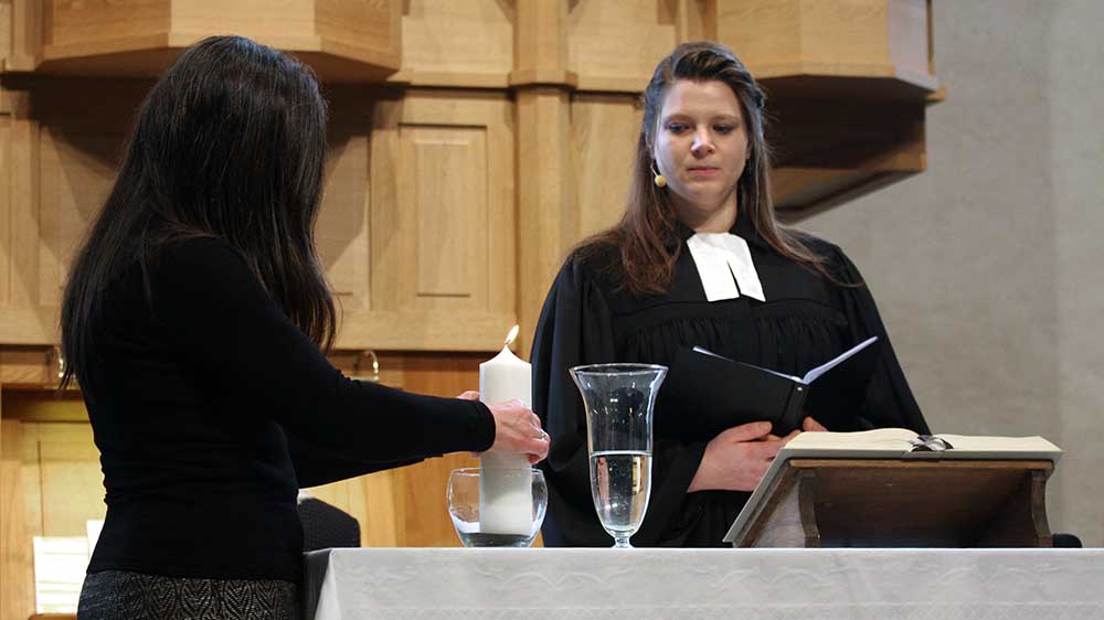 Pfarrerin Angelika Mayer-Ullmann spricht zur Gemeinde, ein Mädchen zündet eine Kerze für Luise an