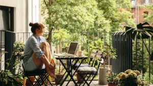 Frau sitzt auf Balkon mit Gartenmöbeln
