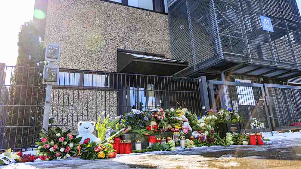 Kerzen und Blumen stapeln sich vor einem Gebäude