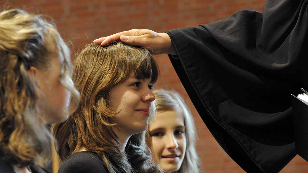 Zur Konfirmation legt der Pastor die Hand auf den Kopf der Konfirmanden