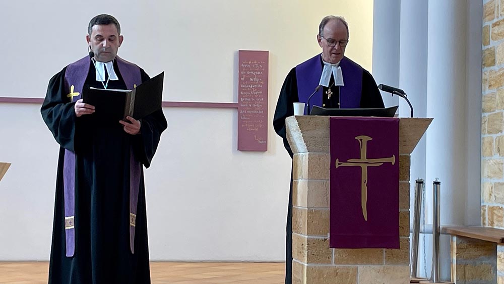 Zwei Männer nebeneinander im Talar in einer Kirche. Der rechte Mann spricht