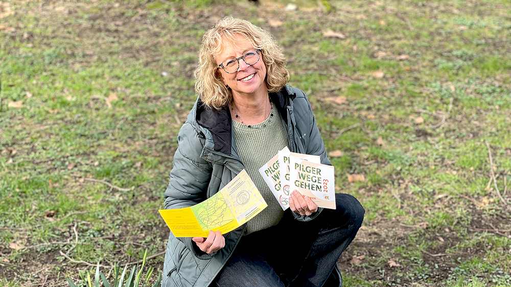 Pilgerbegleiterin Annegret Petersen auf einer Wiese, in den Händen hält sie die Flyer mit dem neuen Programm.