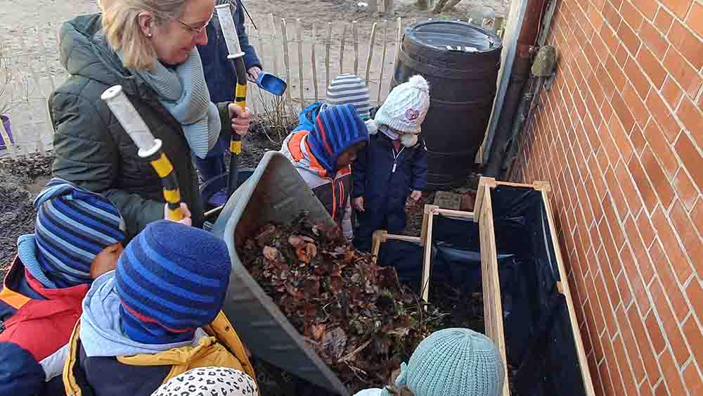 Rein damit! Kitaleiterin Carola Schmidt füllt zusammen mit den Kindern das Beet mit Laub