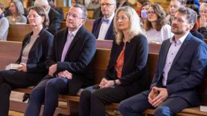 Zwei Männer und zwei Frauen sitzen auf einer Kirchenbank und schauen nach vorn