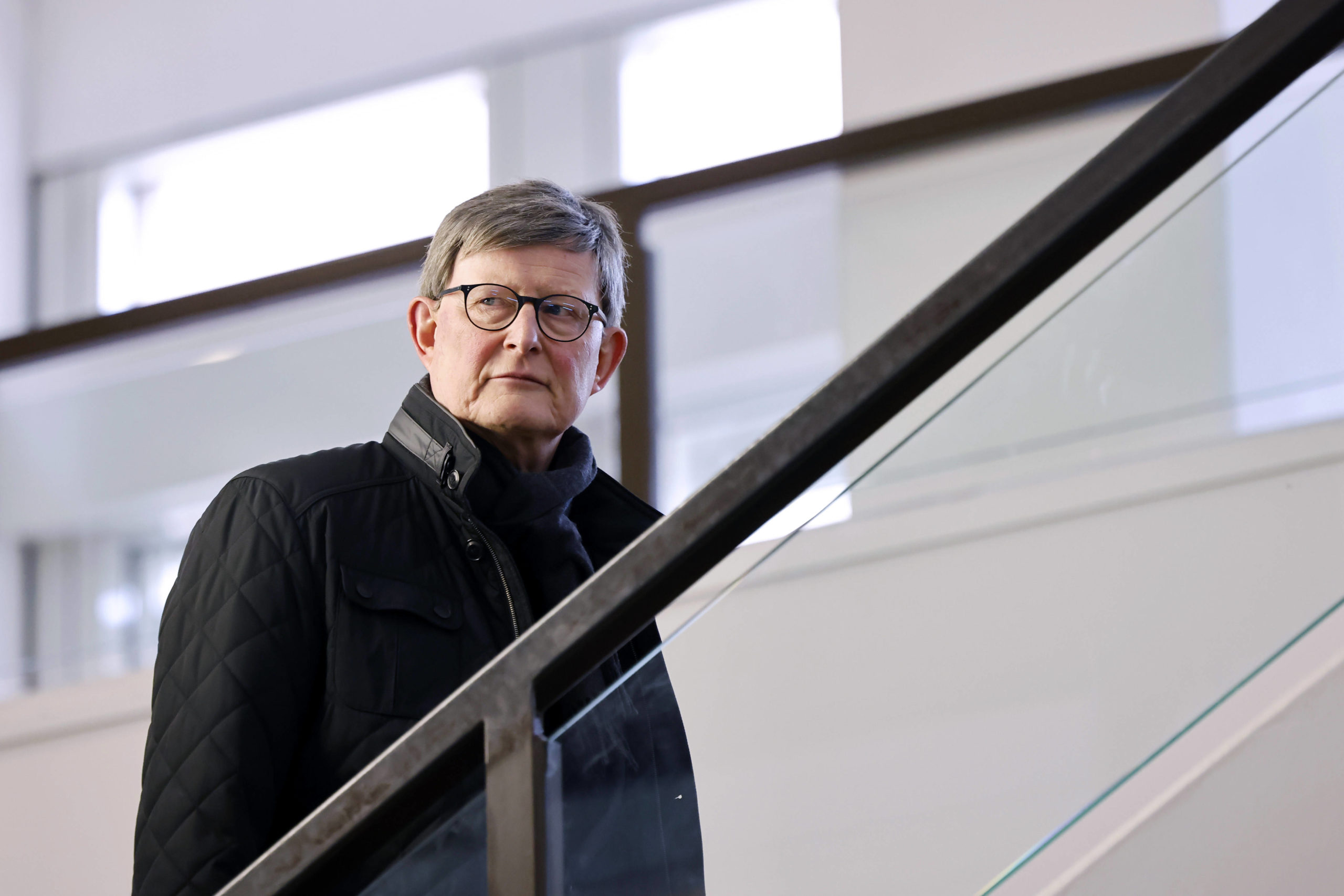 Mann mit schwarzer Jacke und Brille geht eine Treppe rauf
