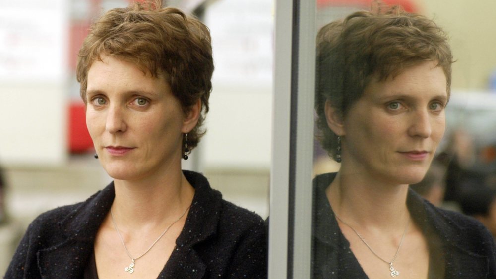 Pehnt steht neben einer Glastür, auf der ihre Spiegelung zu sehen ist