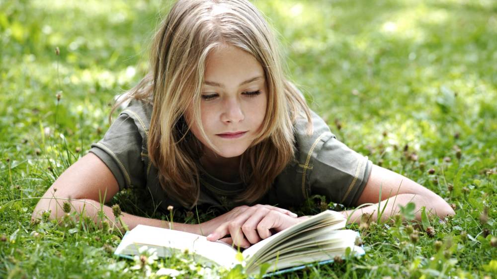 Ein Kind liegt im Gras und liest ein Buch.