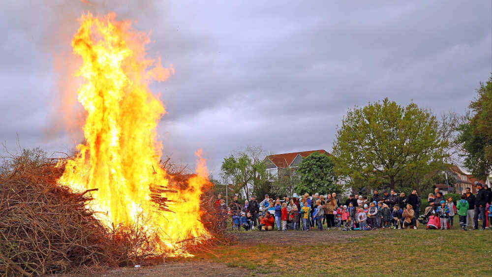 Für das Osterfeuer brennendes Brennmaterial auf einer Wiese mit Menschen im Hintergrund