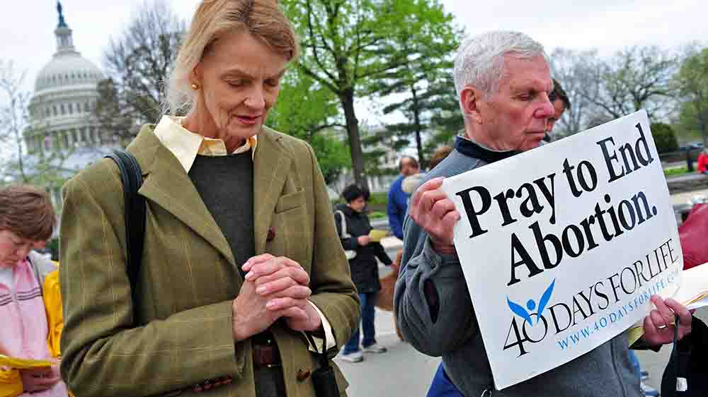 En Mann und eine Frau beten und halten Schilder gegen Abtreibung hoch