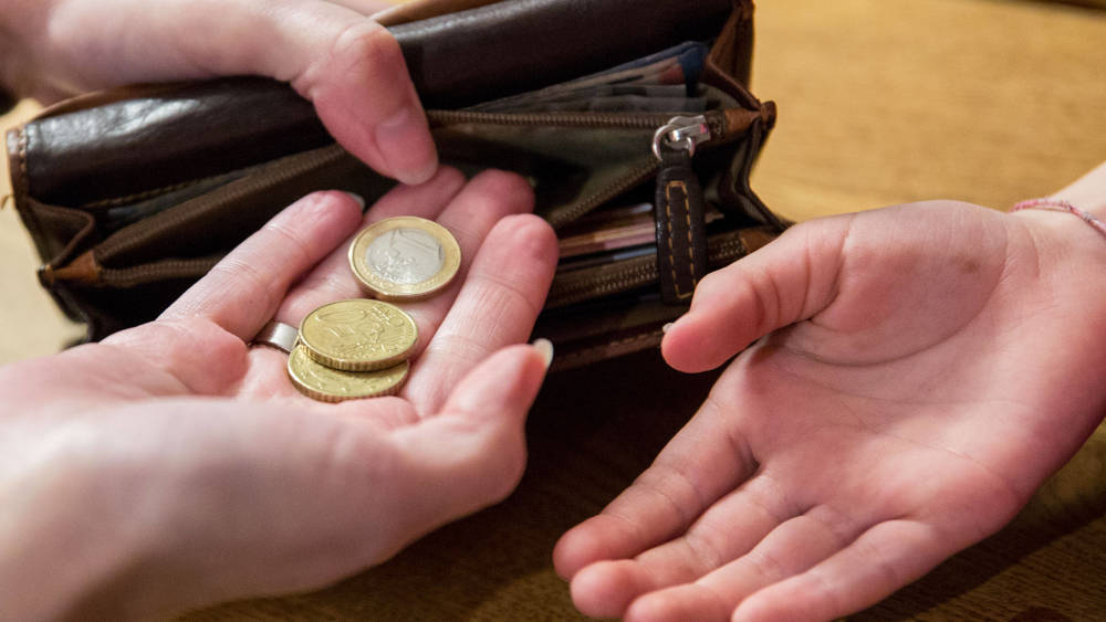 Ein Kind bekommt von der Mutter, die eine Geldbörse in den Händen hält, Ihr Taschengeld auf die Hand