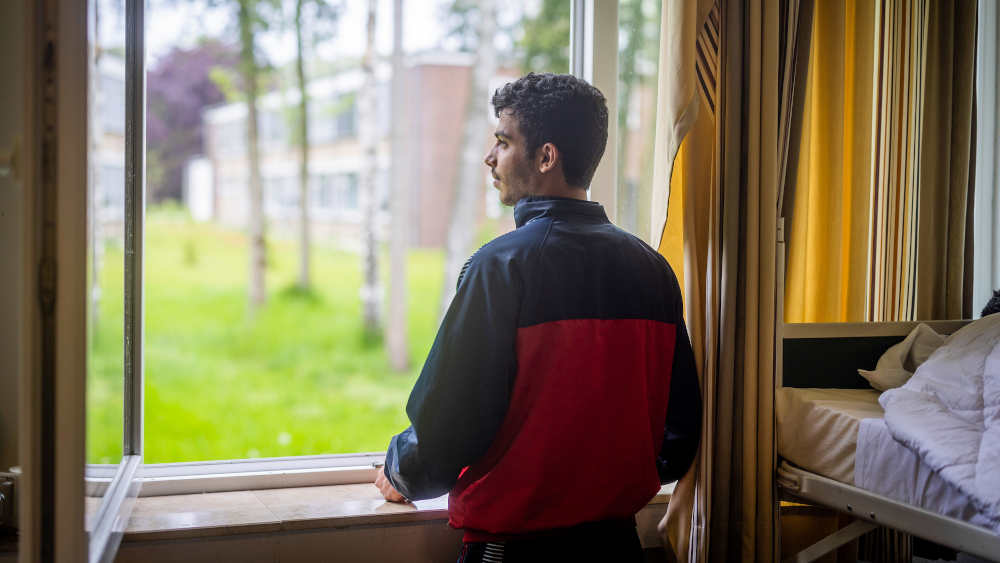 Hassan (19) aus Syrien blickt aus dem Fenster seiner Unterkunft