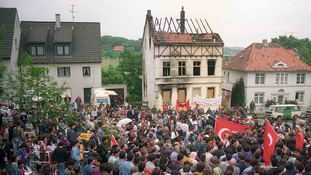 Vor dem abgebrannten Haus versammeln sich im Mai 1993 viele Menschen