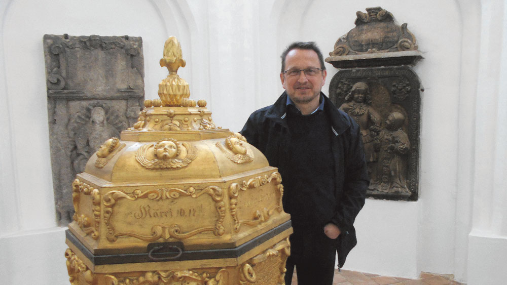 Pfarrer Uwe Weise am Taufstein, hinter ihm Kinder-Epitaphien