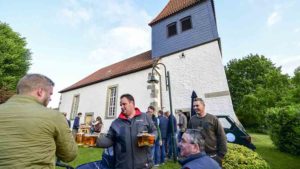 Mehre Menschen sitzen auf Bänke vor einer Kirche und trinken Bier
