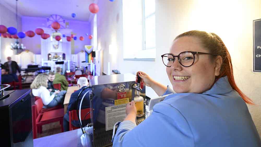 Frau steht an einer Bar und schenkt ein Bier ein
