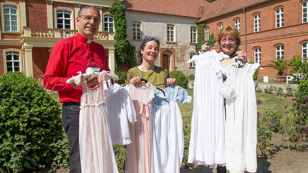 Pfarrer Helmut Kautz, Antje Kahn und Irena Berjas (v.l.) zeigen einige der bisher im Meyenburger Modemuseum abgegebenen Taufkleider
