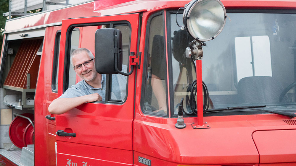 Pfarrer Stefan Mendling im Feuerwehrauto, das fuer Kindergottesdienste eingesetzt werden soll
