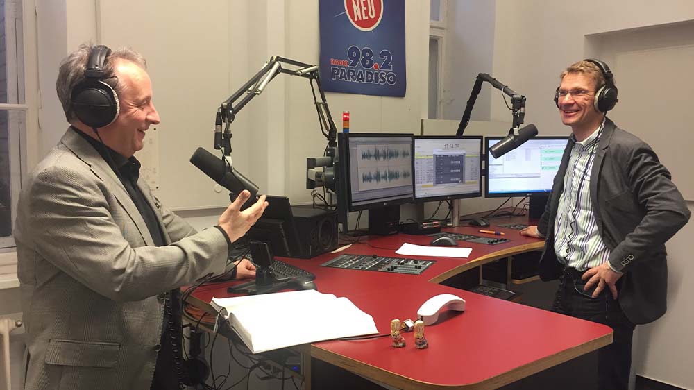 Zwei Männer stehen in einem Radio-Studio und unterhalten sich