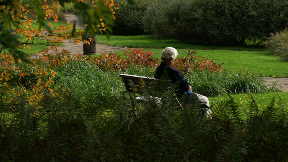 Einsame Seniorin sitzt auf Parkbank