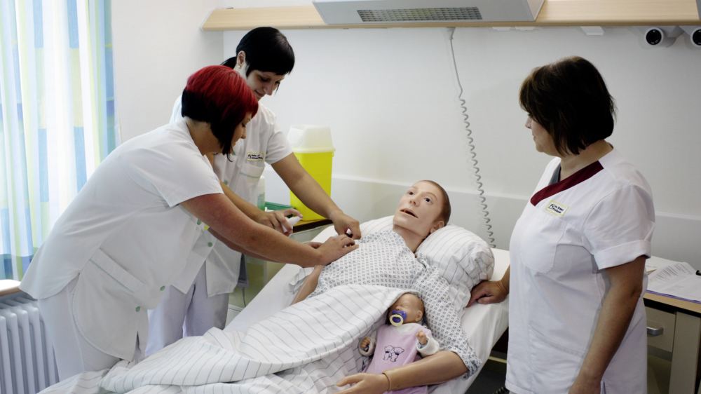 Auszubildende zur Krankenpflegerin lernen an einer Puppe den Umgang mit Patienten