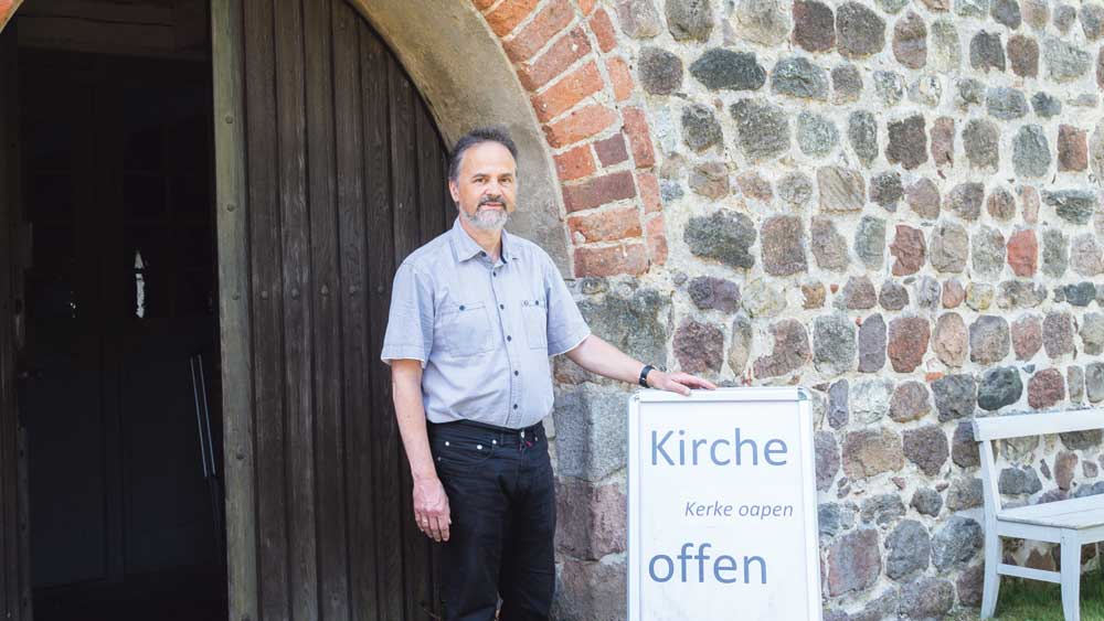 Pfarrer Schönfeld in WIesenburg vor Plakat "Kerke oapen"