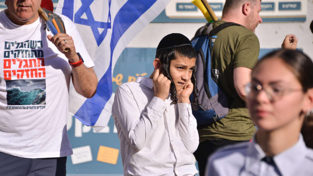Ultraorthodoxer Jugendlicher hält sich während der Demonstration die Ohren zu