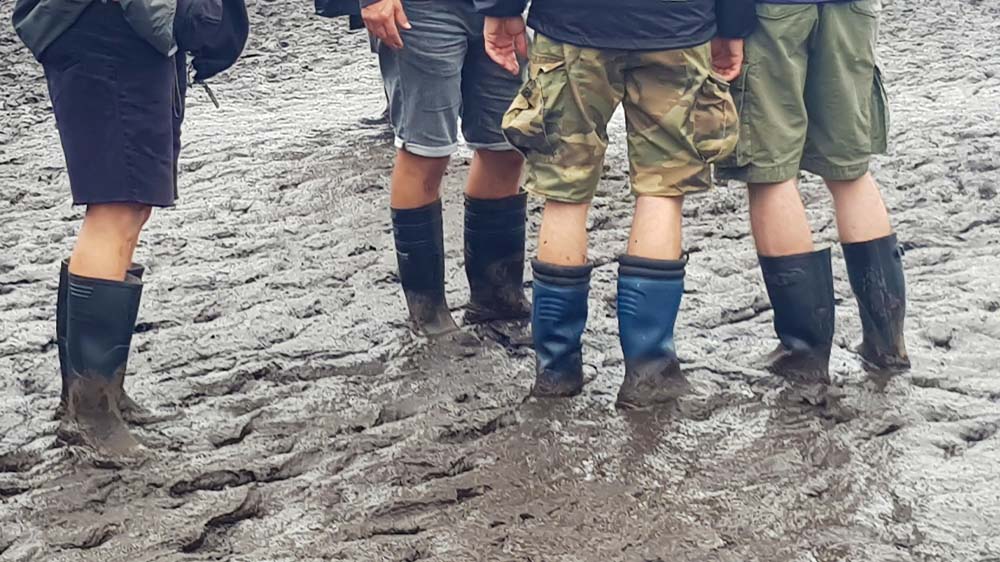Junge Leute stehen mit Gummistiefeln im Schlamm