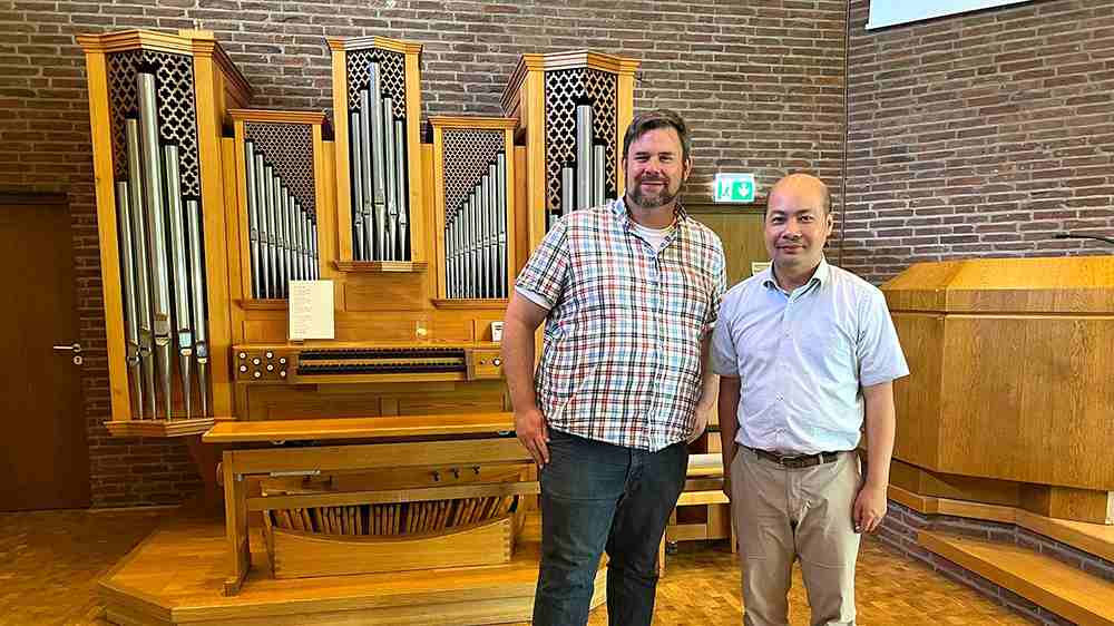 Der Kreuztaler Pfarrer Thies Friederichs und der taiwanesische Organist Haoming Chang stehen vor der Orgel im Kreuztaler Dietrich-Bonhoeffer-Haus.