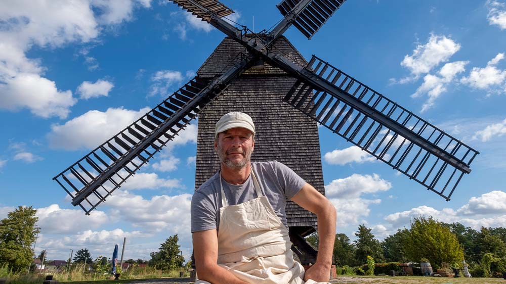 Junger Mann in Müller-Kleidung vor einer Bockwindmühle