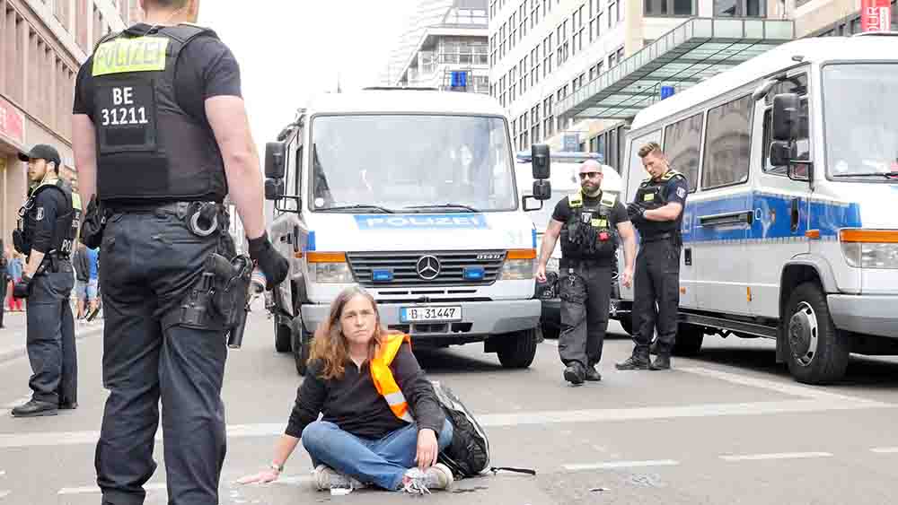 Junge Frau in Warnweste hat sich auf Straße festgeklebt