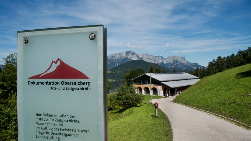 In bergiger Landschaft ein großes Haus und ein Schild zur Ausstellung