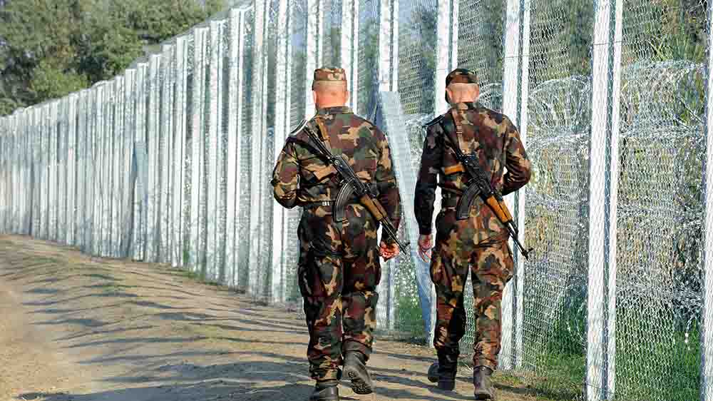 Großer Zaun aus Stacheldraht, neben dem zwei Soldaten laufen