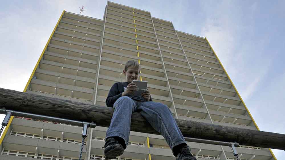 Junge sitzt vor einem Hochhaus