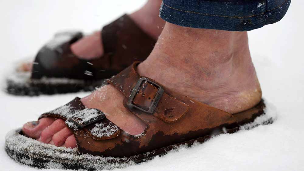 Mann trägt offene Sandalen und läuft durch Schnee