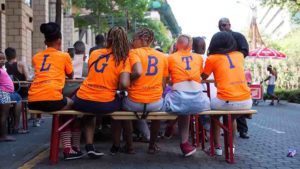 Fünf Personen mit den Buchstabend LGBTQ sitzen mit dem Rücken zur Kamera an einem Tisch