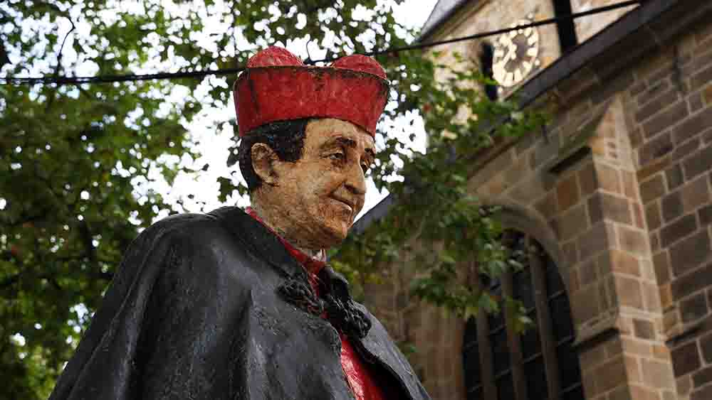 Statue eines Geistlichen im Talar vor einer Kirche