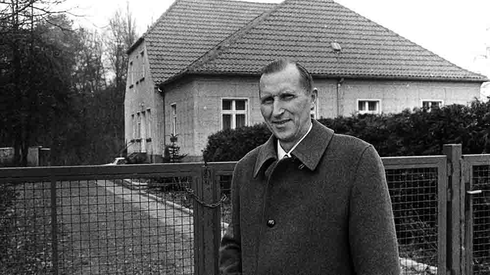 Mann im Mantel steht vor einem großen Wohnhaus