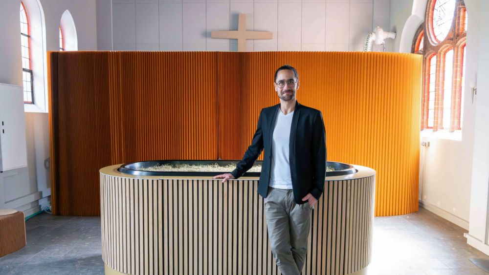Ein Mann steht vor einem badewannenartigen Gefäß in einer Kirche