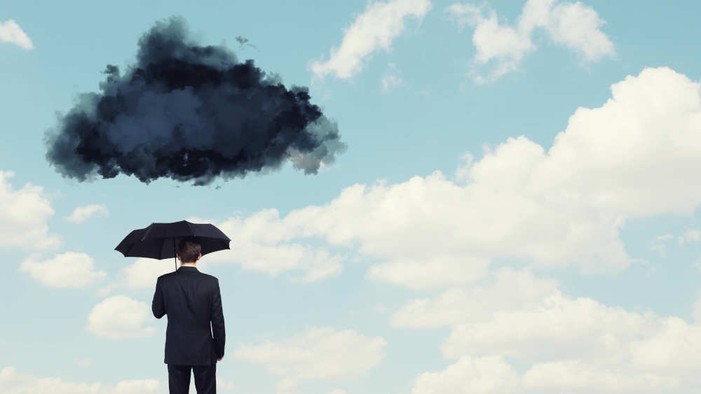 Mann mit Schirm unter dunkler Wolke am blauen Himmel