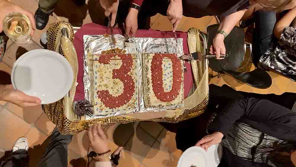Menschen schneiden eine Torte mit einer großen "30" an