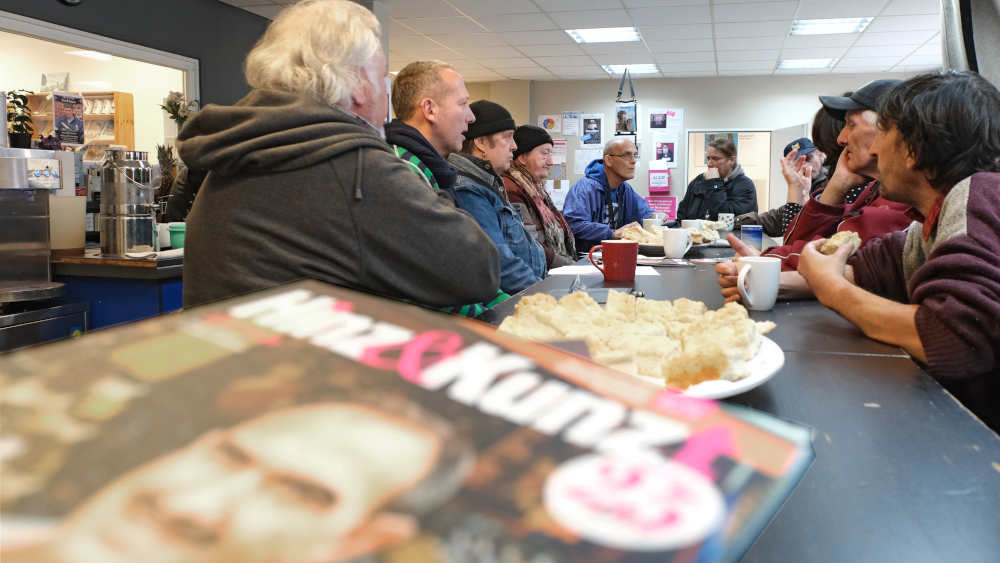 Hamburgs Straßenmagazin "Hinz&Kunzt" liegt auf dem Tisch, dahinter sitzen die Verkäufer