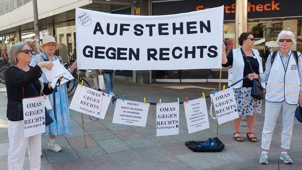 Vier Frauen demonstrieren in einer Fußgängerzone gegen Rechtsextreme. Sie halten ein großes weißes Transparent mit der Aufschrift "Aufstehen gegen Rechts".