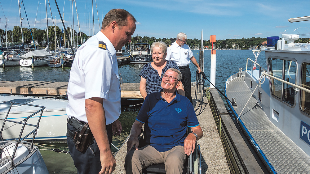 Hospizklient im Rollstuhl wird in ein Polizeiboot getragen