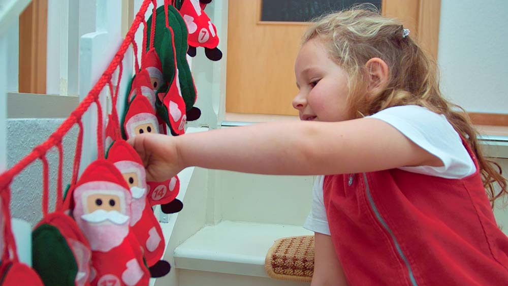 Kind greift in einen Adventskalender, der aus Weihnachtsmännern besteht, die an einer Schnur hängen