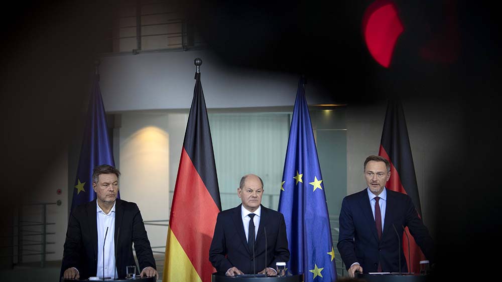 Drei Männer bei einer Pressekonferenz, darüber groß das rote Licht einer Kamera
