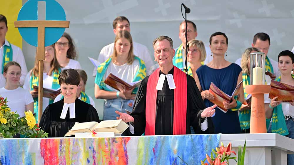 Mann im Talar und mit rotem Schal steht auf Bühne