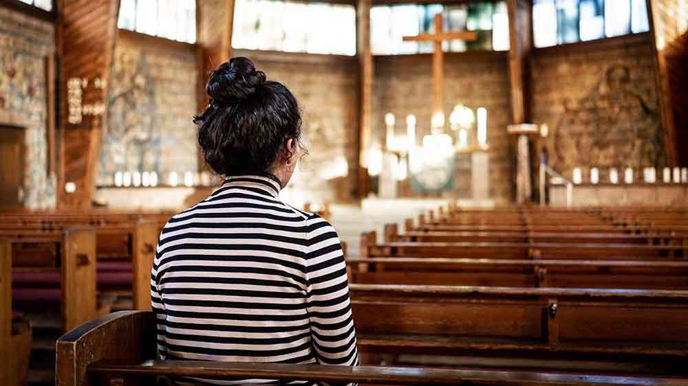 Frau im schwarz-weiß gestreiften Pullover sitzt mit dem Rücken zur Kamera auf einer Kirchenbank