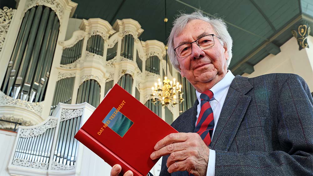 Älterer Mann mit plattdeutscher Bibel in der Hand vor einer Orgel