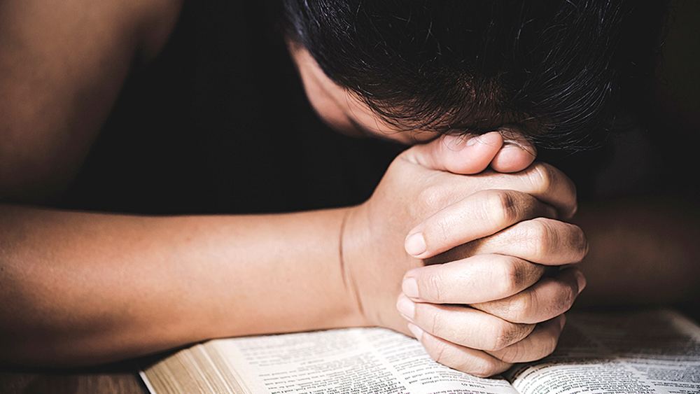 Eine Person betet verzweifelt auf einer aufgeschlagenen Bibel.